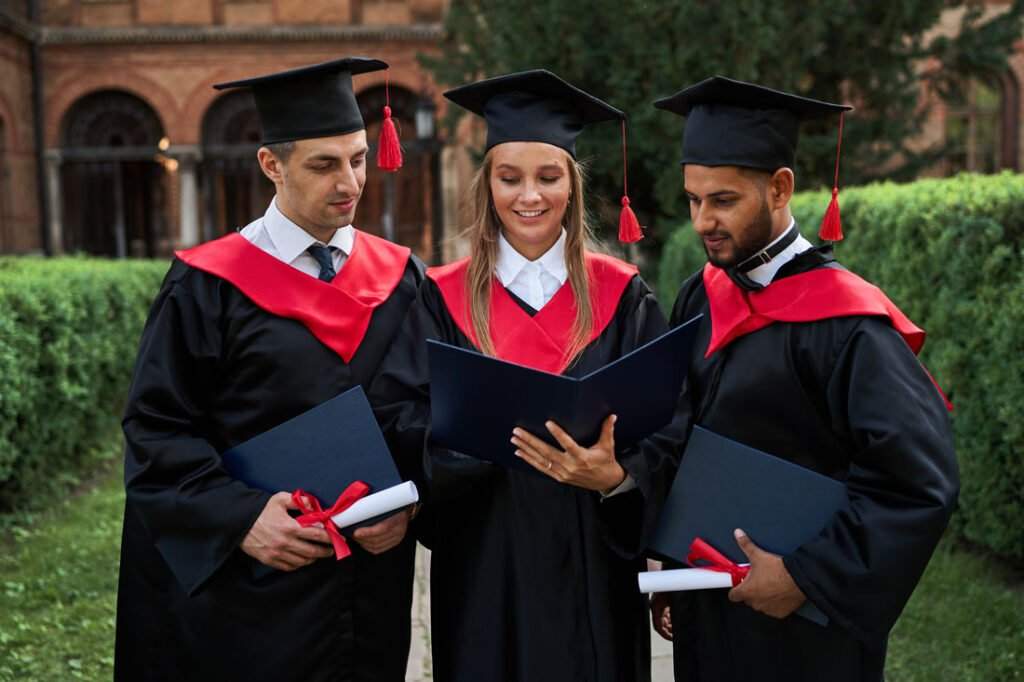 three graduate friends graduation robes looking their diploma campus 1